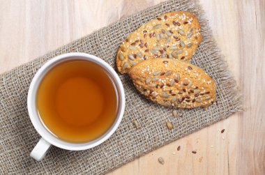 Ayçiçeği tohumu ve susam çuval bezi üzerinde çay ve yulaf ezmesi kurabiye fincan ahşap arka planda, üstten görünüm bulunur