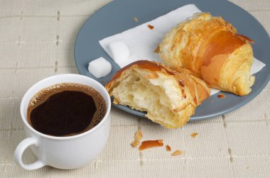 Bir fincan kahve ve bir masa örtüsü ile bir tabloda gri bir plaka üzerinde yarım çörek. Kahvaltı veya break Tema