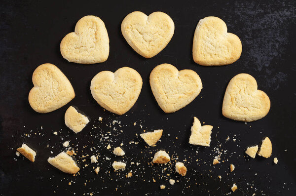 Cookies in the shape of a heart whole end broken on old black metal background, top view