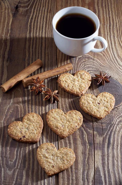 Oatmeal cookies in the shape of a heart,  cup of coffee, cinnamon and anise stars on old wooden table
