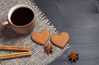 Kaba kumaş kopya alanı siyah bir ahşap zemin bulunan iki kalp şeklinde zencefilli kurabiye, fincan kahve, tarçın ve anason yıldızlı