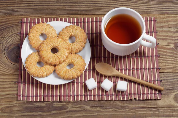 木製のテーブルの上の竹のナプキンの朝食のプレートにお茶と甘いクッキーのカップ — ストック写真