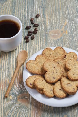 Plaka ve kahve eski ahşap masa üzerinde bir kalp şeklinde kurabiye