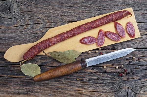 苗条的熏制香肠 胡椒和月桂叶在切割板上位于木制背景 顶视图 — 图库照片