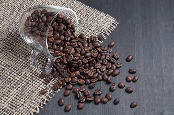 Kaffebönor Utspridda Från Glas Kopp Svart Trä Yta Med Säckväv — Stockfoto