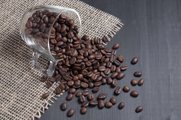 Grãos Café Espalhados Uma Xícara Vidro Uma Superfície Madeira Preta — Fotografia de Stock