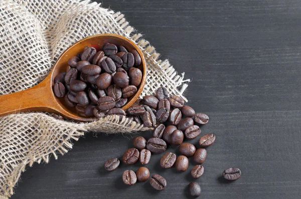 Kahve çekirdekleri bir tahta kaşık ve yakın çuval bezi ile siyah bir arka plan üzerinde yer almaktadır. Metin için yer