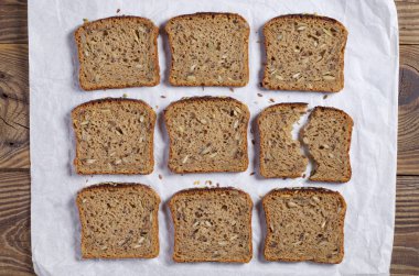 Dilim ekmek farklı tohumları ile beyaz kağıt, ahşap masanın üstünde, üstten görünüm bulunur