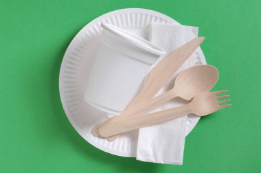 Yeşil arka planda tek kullanımlık tabaklar, üst manzara. Cam, tabak, kaşık, çatal, bıçak.