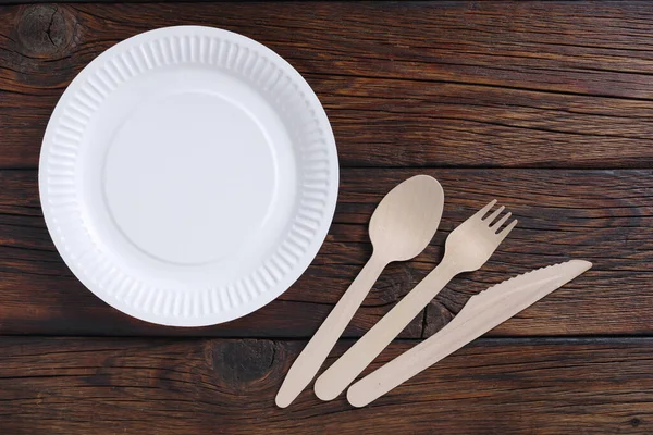 Paper plate, wooden fork and knife on wood, top view. Disposable tableware