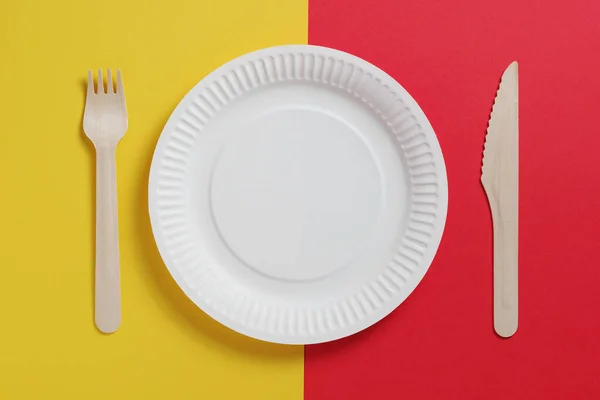 Disposable plate and wooden cutlery on two-tone background, top view