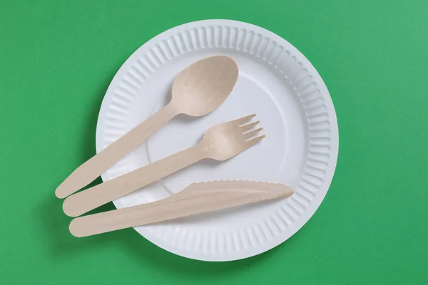 Wooden cutlery on a disposable paper plate on green background, top view