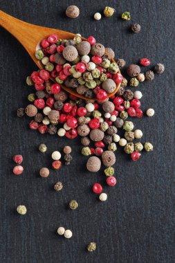 Renkli biberler ahşap kaşıkta karışıyor ve yakın plan siyah taş arka plan, üst görünüm üzerine dağılıyor.