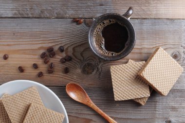 Bir fincan sıcak kahve ve kahvaltıda kaynamış sütle birlikte gofret, ahşap masa, üst manzara.