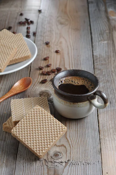 Cup of hot coffee and wafers with boiled condensed milk for breakfast on wooden table