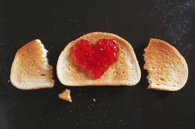 Kalp şeklinde çilek reçeli ve eski siyah metal tepside iki dilim kızarmış ekmek.