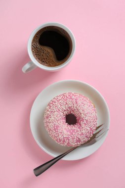 Pembe çörekler bir tabağa serpiştirilmiş ve arka planda bir fincan kahve, üst manzara.