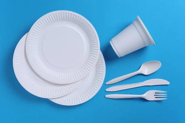 Disposable tableware and cutlery on blue background, top view