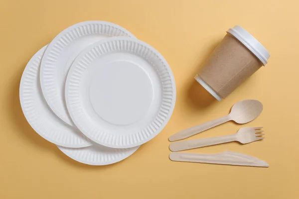 Disposable tableware and wooden cutlery on yellow background, top view