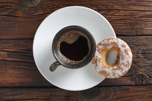 Cup of coffee and glazed bagel on wooden background, top view