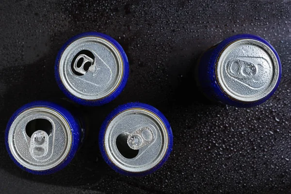 Opened beer cans in drops of water on black background, top view