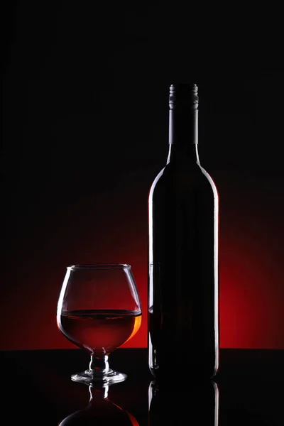 Botella de vino tinto y copa sobre fondo oscuro — Foto de Stock