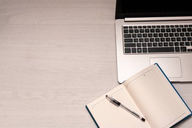 Beyaz ahşap masa üzerinde siyah kalem ve gümüş dizüstü bilgisayar ile açılan defter, üst görünüm, spazm kopya
