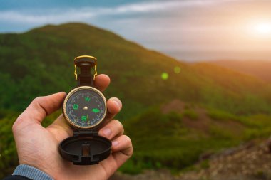 Seyahat, kamp, orienteering ve navigasyon konsepti - siyah manyetik pusula yakın çekim bir adamın elinde, bulanık manzara arka plan