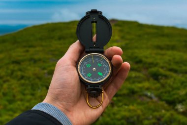 Seyahat, kamp, orienteering ve navigasyon konsepti - siyah manyetik pusula yakın çekim bir adamın elinde, bulanık manzara arka plan