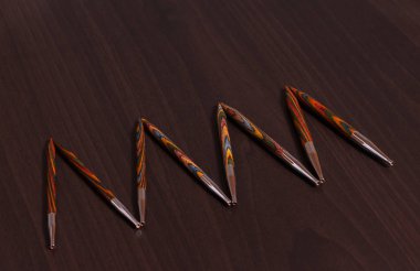 Koyu ahşap bir masa üzerinde bir satır da ortaya konan farklı boyutlarda çok renkli bambu örgü iğneleri