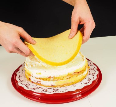 Kırmızı plastik tepside katmanlı pasta yapan kişi.