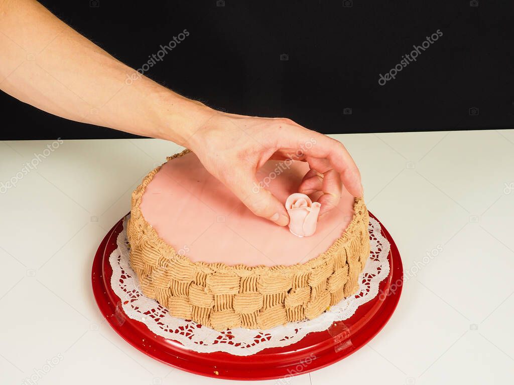 Baker adding a pink rose onto a pink marzipan coverd layer cake