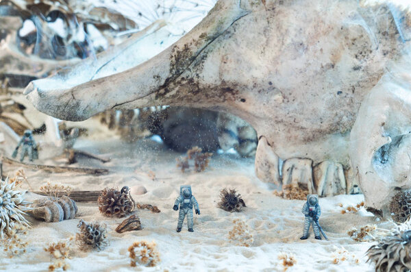 Photo of toy astronauts, giant skulls, smoke and sand. Dead planet, polluted air or environmental  concept.