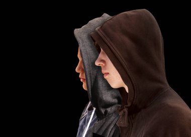 Two troubled teenage boys with black hoodie standing next to each other in profile isolated on black background clipart