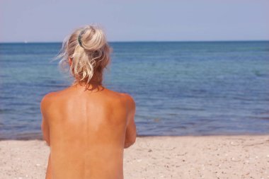 Kumsalda güneş ışığı bulunan oturma ve arkadan gördüm deniz - seyir güzel sarışın güneş tabaklanmış üstsüz kadın