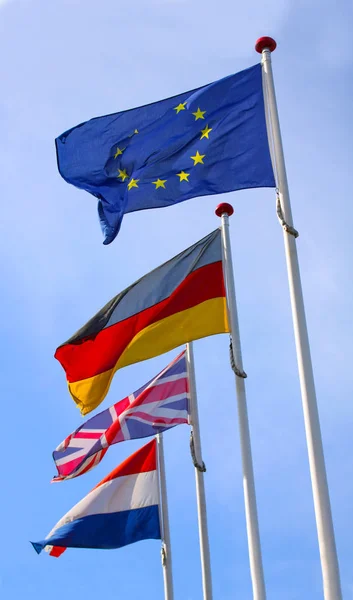 Flags from England, United Kingdom, Germany and France waving from flagpoles together with the EU, European Union, flag against a blue sky.