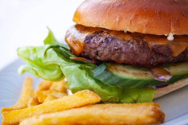 Büyük, sulu bir hamburger ve beyaz tabakta kızarmış patates. Son derece yakın plan görüntü.