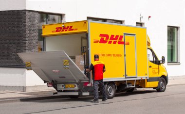 Üniformalı teslimatçı bir DHL kamyonunda bagaj yükleyicisini açıyor. Kurye, paket ve ekspres posta servisi. Paketler kamyonun içinde görünüyor. Kopenhag, Danimarka - 22 Haziran 2020.
