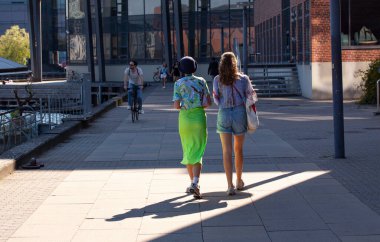 İki kız yan yana yaya caddesinde güzel renkli giysiler içinde yürüyorlar. Biri uzun yeşil elbise ve diğeri seksi kot pantolon giyiyor. Kopenhag, Danimarka - 27 Haziran 2020.