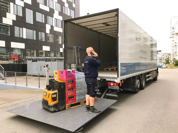 İçecekler boşaltılırken cep telefonuyla konuşan teslimatçı bir teslimat kamyonunun bagajındaki forkliftle ofis binasının önünde bekliyor. Kopenhag, Danimarka - 10 Temmuz 2020. 