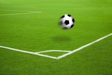 Futbol sahasında beyaz çizgili, köşe işaretli bir futbol topu. Doymuş yeşil çimenler ve havada hareket bulanıklığı ve gölge ile futbol.