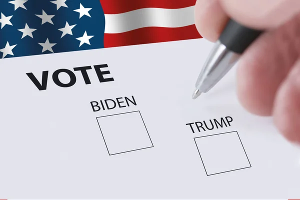 鉛筆を持っているぼやけた手で2020年の大統領選挙投票とバイデンやトランプに投票するためのチェックボックス 背景にアメリカ国旗が振ってある — ストック写真