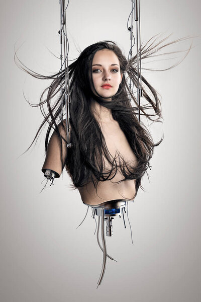 Cyborg woman suspended by metal clamps with cables and electrical wires showing below torso and arms. Conceptual of futuristic bionics and artificial intelligence