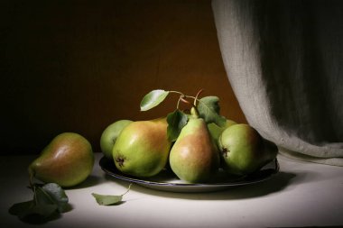 Pembe kenarlı yeşil armutlar cam bir tabakta yatıyor..