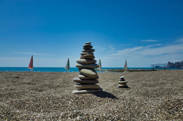 Stones pyramid on pebble beach symbolizing stability, zen, harmony, balance. Shallow depth of field. Beach umbrellas in the background