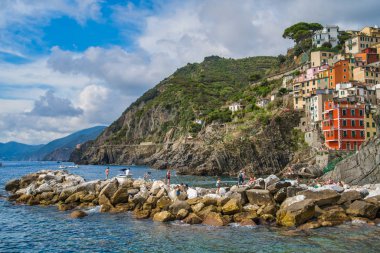 Cinque Terre, İtalya - 17 Ağustos 2019: Ligurian Denizi 'nin kayalık kıyılarındaki güzel renkli evler. Dağa ağaç serpmek. Turistler kayalarda güneşlenir.
