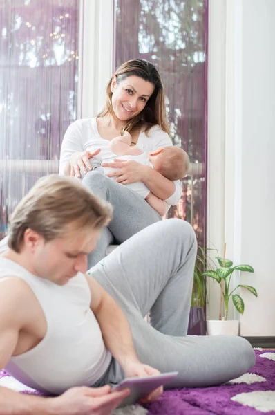 幸せな親 床に置くとタブレットで遊んでの父 母の乳房がバック グラウンドで彼女の男の赤ちゃんをフィード — ストック写真