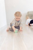Aranyos csecsemő baba fiú mászik a padlón otthon, és játék-val színes labda