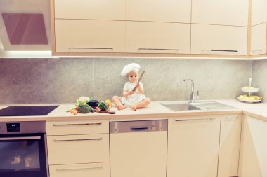 Bebek sebze mutfakta arasında oturan çocuk ve yemek pişirmek için hazırlar