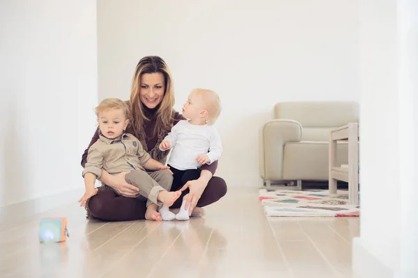 Щаслива мати сидить на підлозі з двома немовлятами і грає . — стокове фото